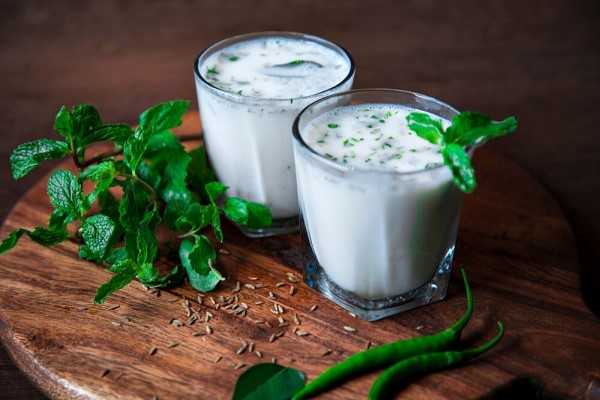 Two full glass of Buttermilk kept on Brown table with green herbs