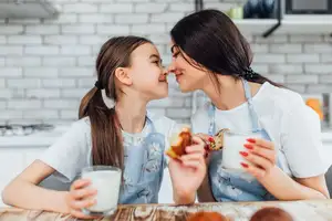 mom and daughter smiling while tasting their muffins and drinking milk
