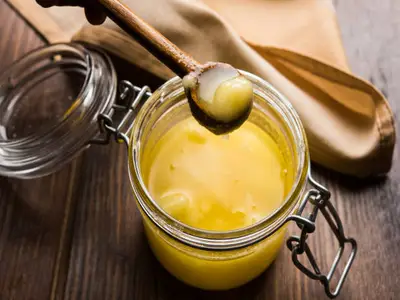 jar and spoon of deshi ghee (clarified butter) on brown wood table