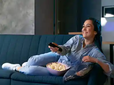 Young woman eating popcorn while watching tv at home
