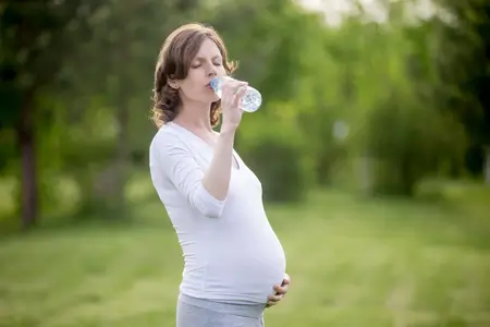 Pregnant woman drinking water in natural park