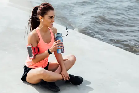 Sport woman sitting near lake with water bottle