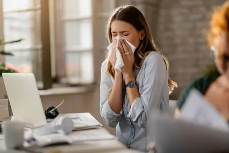 young-woman-sick-with-flu-and-sneezing-while-working-in-office